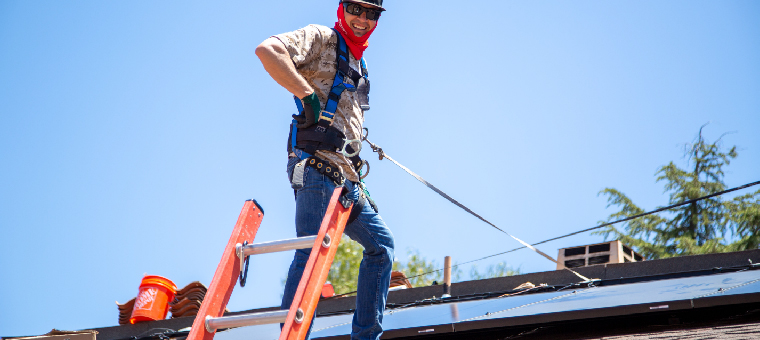 Installer on roof smiling near solar panels sunny day.